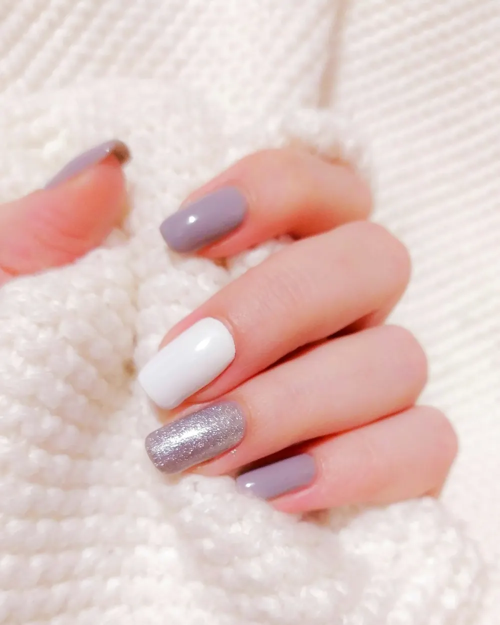 Dłonie z manicure w kolorach nude na tle jasnego swetra